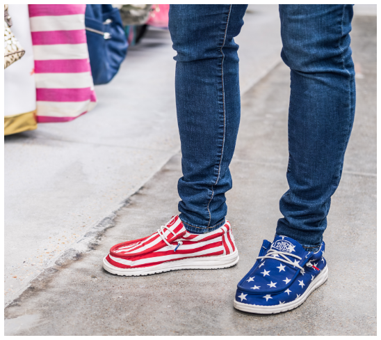 Person wearing jeans and red, white, and blue American flag sneakers inside thrift store.